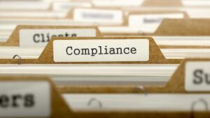 A file folder in a filing cabinet is labeled "Compliance."