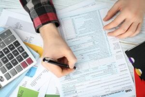 Top-view photo of a calculator, miscellaneous papers and a person completing tax documents