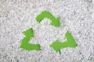 A recycle symbol is made inside a heap of shredded white paper on a green surface.