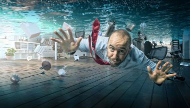 A business person is swimming in a flooded office.