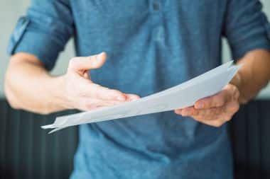 A person in a blue shirt is holding out a piece of paper as proof.